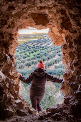 A vertical shot of a girl tourist standing at the entrance of a cave