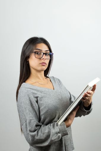 A Young woman in optical glasses wearing glasses and holding a book against white background