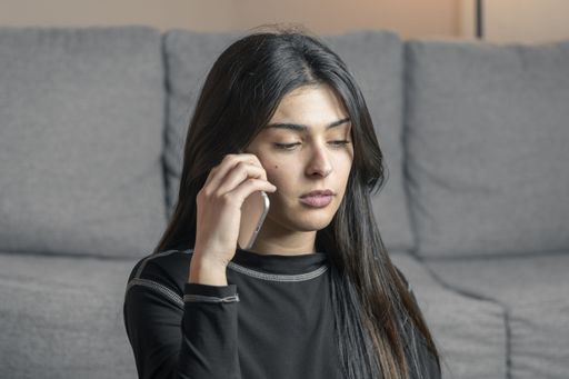 A young Latina woman with long dark hair sits in the living room, talking on the phone