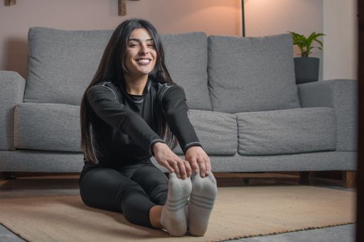 Young woman in athletic wear stretching on a rug in a cozy living room setting.