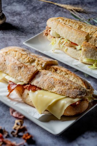 A vertical shot of delicious sandwiches with cheese and bacon in rectangular plates at a restaurant