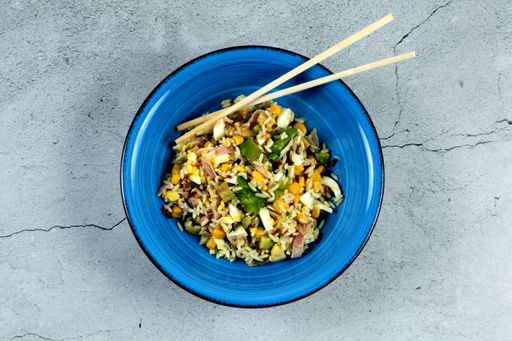 A top view of a blue ceramic bowl containing rice, corn, and salad with chopsticks on it