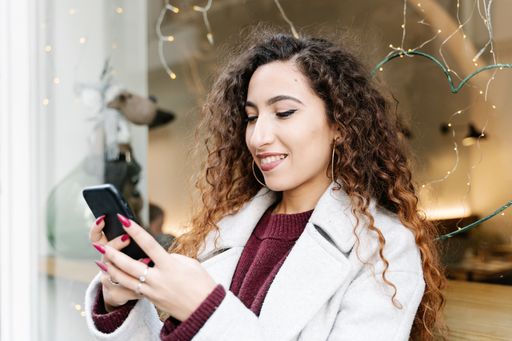 A shallow focus shot of a female leaning against a window while using her smartphone