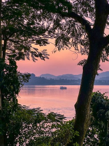 Serene lake view at sunset with silhouetted trees and distant hills, creating a tranquil scene.