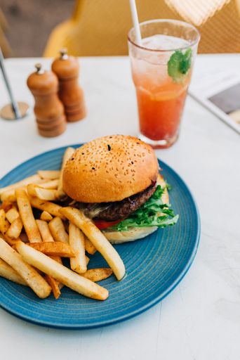 A vertical shot of a delicious burger and some french fries and a glass of cocktail on a table