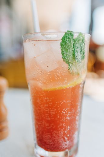 A vertical shot of a glass of a delicious orange cocktail with mint leaves with ice on a table