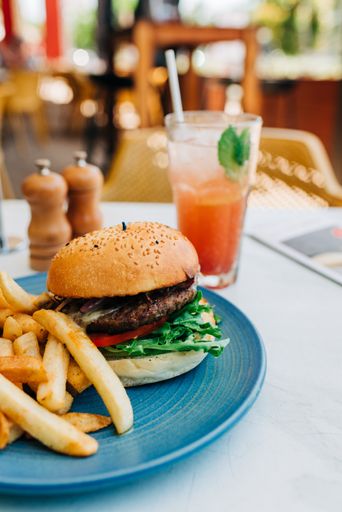 A vertical shot of a delicious burger and some french fries and a glass of cocktail on a table