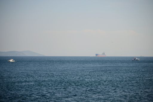 A misty spring day at a beach with boats hovering over the wavy sea waters