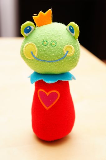 A vertical shot of a soft colorful frog toy isolated on the wooden table