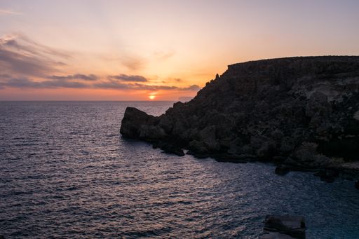Sunset on a beautiful spring day as seen from Anchor Bay, Mellieha, Malta. The sun setting over the horizon with some clouds and calm sea.