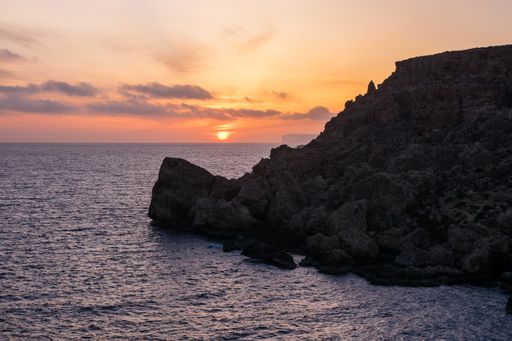 Sunset on a beautiful spring day as seen from Anchor Bay, Mellieha, Malta. The sun setting over the horizon with some clouds and calm sea.