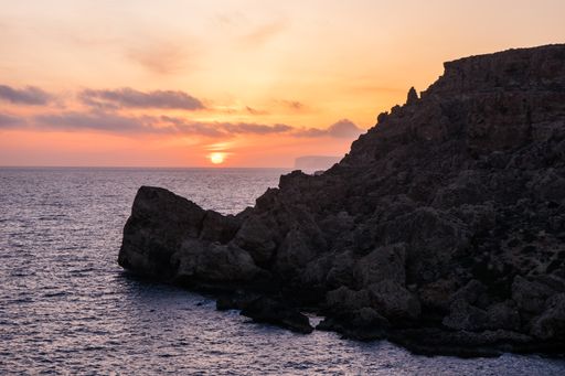 Sunset on a beautiful spring day as seen from Anchor Bay, Mellieha, Malta. The sun setting over the horizon with some clouds and calm sea.