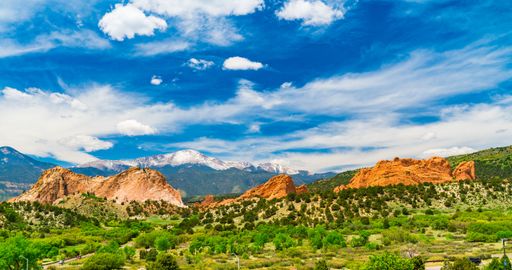 Scenic view of Garden of the Gods with red rock formations and snow-capped mountains under a vibrant blue sky in Colorado.
