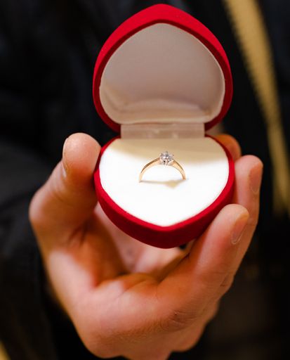 A vertical shot of a gold engagement ring in a heart-shaped box in a male hand