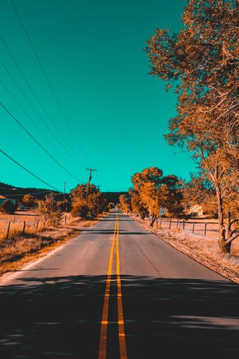 A vertical shot of an empty asphalt road with yellow indicator lines under a clear blue sky