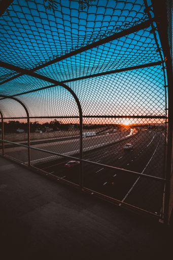A vertical shot of an expressway against a beautiful sunset sky as seen through a caged footbridge