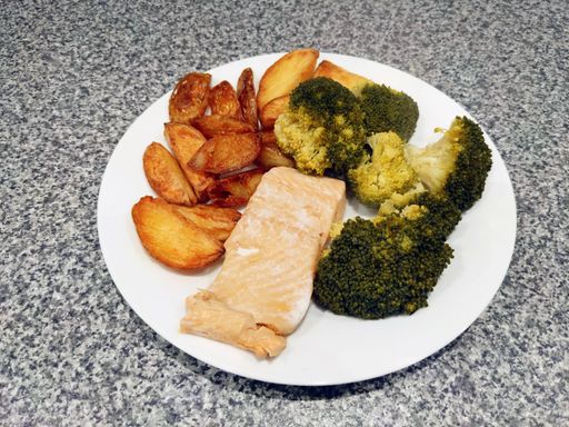 A closeup shot of a white plate filled with cooked fish, broccoli, and potatoes on the table