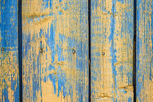 A closeup of old blue and yellow wooden boards with peeling paint