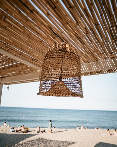 A vertical shot of a lamp hanging from a straw ceiling on the beach background