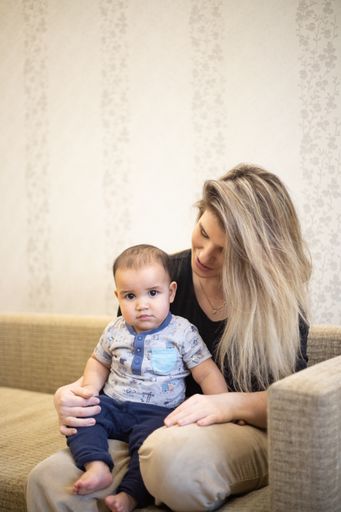 A vertical shot of a little child sitting on his mother's lap on the couch under the lights in a room