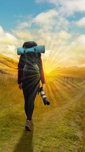 A magic, rear view of a female hiker with a backpack and camera walking to the sun