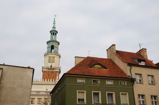 A low angle shot of the city hall of Poznan behind some houses under the cloudy sky
