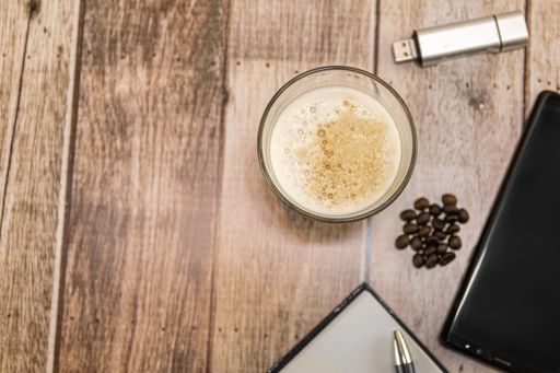 A top view of a glass of iced coffee, coffee beans, and other objects on a wooden table - copy space