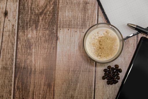 A top view of a glass of iced coffee, coffee beans, and other objects on a wooden table - copy space