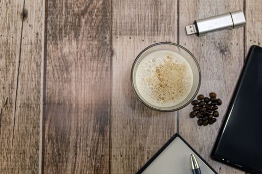 A top view of a glass of iced coffee, coffee beans, and other objects on a wooden table - copy space
