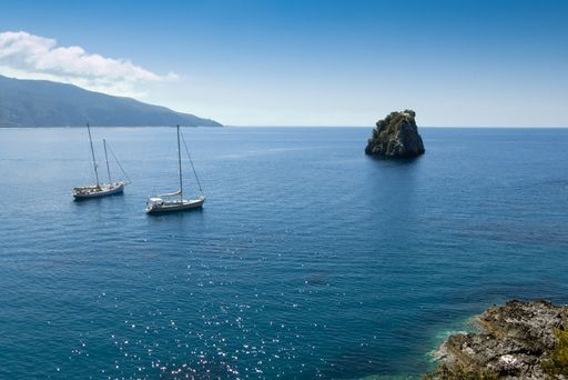 A beautiful view of large blue water, boats and mountains on the horizon under a sunny sky in Centola, Italy