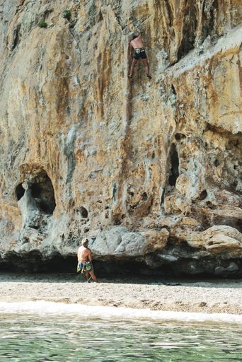 A vertical shot of a free climber in action while climbing a rocky wall  Cilento, Campania, Italy