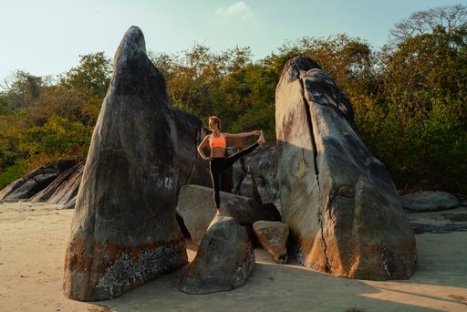 A young slim attractive Caucasian woman on a huge rock doing stretching exercises in nature on a sunny day