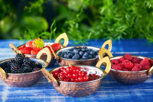 Fresh different types of berry in bowls on blue table with green background
