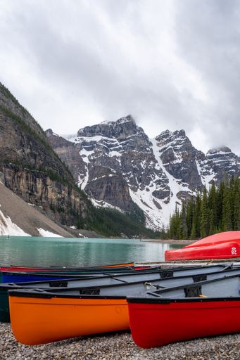 A vertical shot of canoes on the shore of Moraine Lake surrounded by snowy hills in Canada