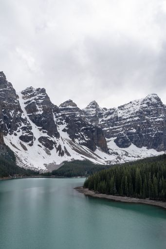 A vertical shot of Moraine Lake surrounded by rocky hills covered in the snow in Canada