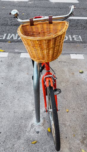 A vertical shot of a red, retro bicycle with a straw basket parked on a bike parking area