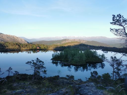 A scenic shot of a lake surrounded by mountain forests under the blue sky