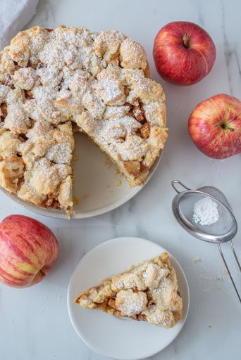 A top view of a sliced apple cinnamon pie with sugar powder on a plate on the table