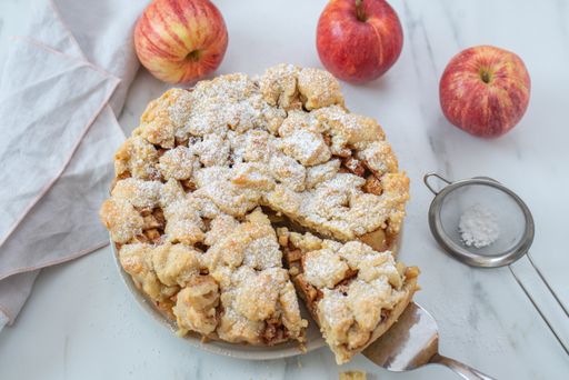 A closeup of a sliced apple cinnamon pie with sugar powder on a plate on the table