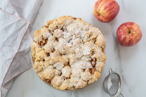 A top view of a whole delicious apple cinnamon pie with sugar powder on a plate on the table