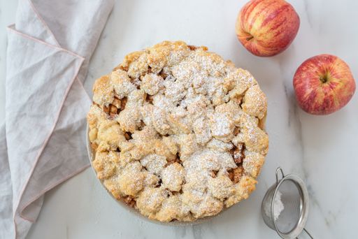 A top view of a whole delicious apple cinnamon pie with sugar powder on a plate on the table