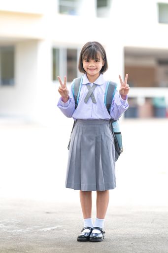 A vertical shot of an adorable cute child schoolgirl posing with peace signs