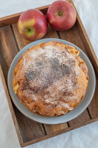 A vertical shot of a whole homemade apple pie with sugar powder on a plate on a tray