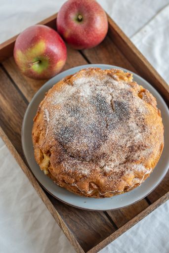 A vertical shot of a whole homemade apple pie with sugar powder on a plate on a tray
