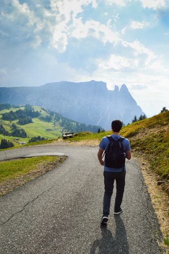 A vertical shot of the man walking along the rural road. Alpe di Siusi, Dolomites, Italy.
