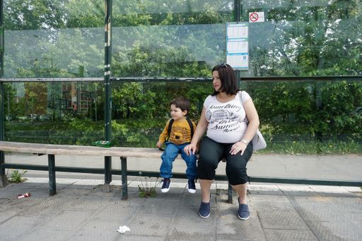 A pregnant woman with her cute boy sitting at the bus stop during the daytime