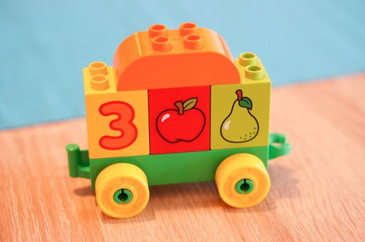 A close-up shot of a colorful Lego Duplo cart with blocks on a wooden table in the children room