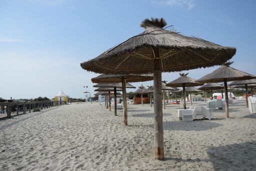 A close-up shot of a row of straw beach umbrellas against a blue sky on a sunny day in Romania