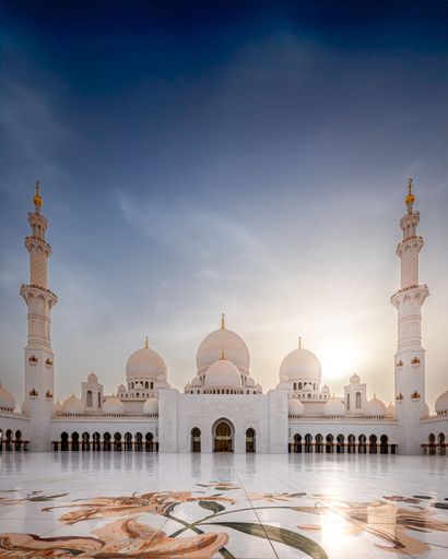 Stunning view of Sheikh Zayed Grand Mosque in Abu Dhabi against a clear sky, showcasing its intricate architecture and marble courtyard.