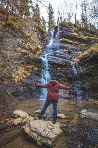 The vertical shot of a man standing near the Cascada Uguna waterfall in the forest Otzarreta, Basque Country